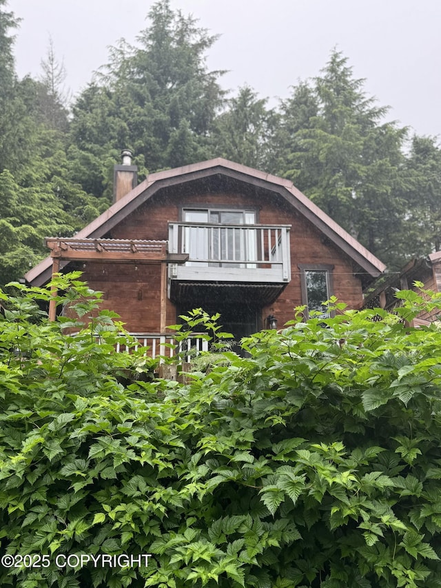 view of side of property with brick siding, a chimney, and a balcony