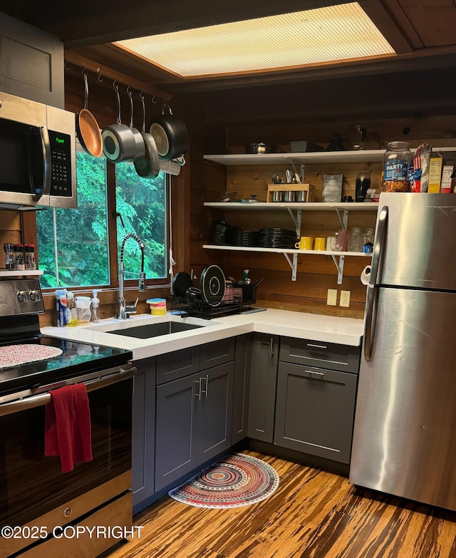 kitchen featuring gray cabinets, stainless steel appliances, light countertops, open shelves, and a sink