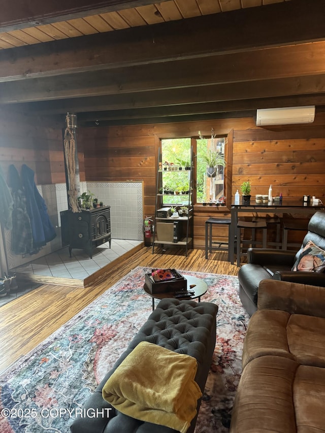 living room featuring wooden walls, wood finished floors, beam ceiling, a wall mounted air conditioner, and a wood stove