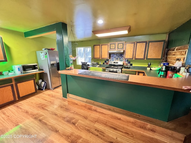 kitchen with under cabinet range hood, stainless steel appliances, a peninsula, a breakfast bar, and light wood finished floors