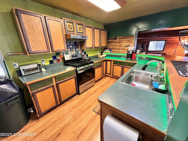 kitchen featuring a toaster, light wood-style flooring, stainless steel gas range, under cabinet range hood, and a sink