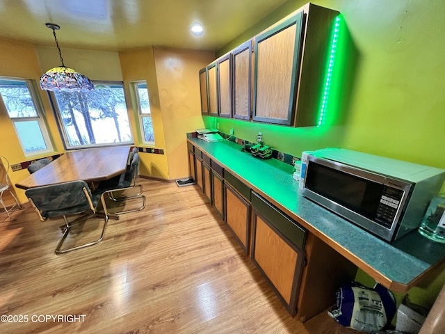 kitchen with light wood-style floors, stainless steel microwave, and decorative light fixtures