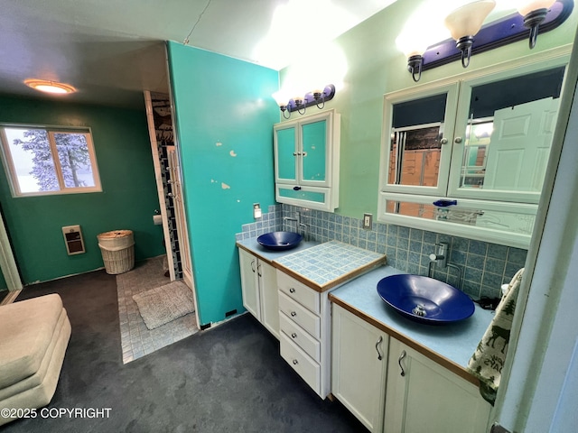 bathroom with heating unit, two vanities, decorative backsplash, a sink, and walk in shower