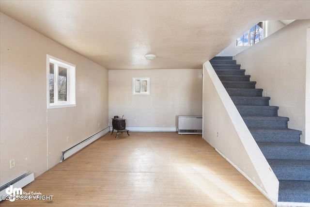 basement featuring stairway, a baseboard heating unit, baseboards, and wood finished floors