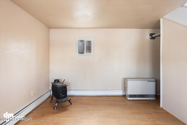 unfurnished room featuring wood finished floors, a baseboard heating unit, and a wood stove