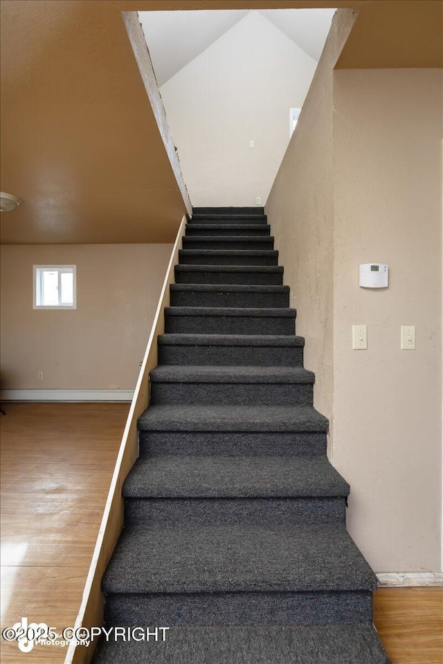 stairway with wood finished floors, baseboards, and vaulted ceiling