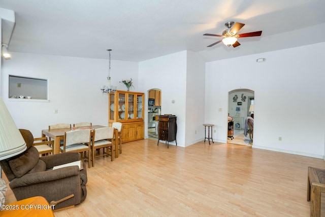 living area featuring arched walkways, ceiling fan with notable chandelier, baseboards, vaulted ceiling, and light wood-style floors