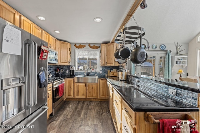 kitchen featuring dark stone countertops, dark wood-style floors, a sink, appliances with stainless steel finishes, and tasteful backsplash