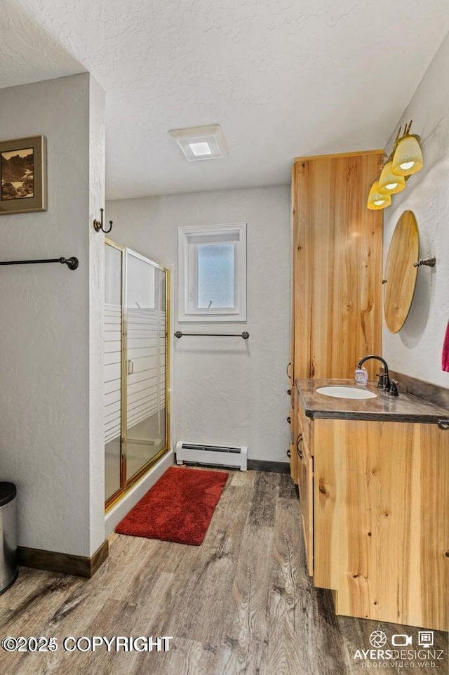 bathroom with vanity, wood finished floors, a stall shower, a textured wall, and baseboard heating