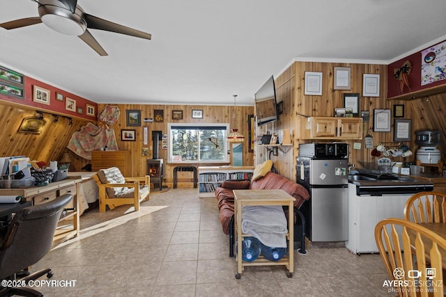 interior space featuring tile patterned floors, a wood stove, wooden walls, and a ceiling fan