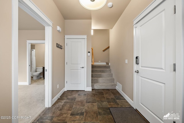 entrance foyer with visible vents, baseboards, stone finish floor, stairway, and dark carpet