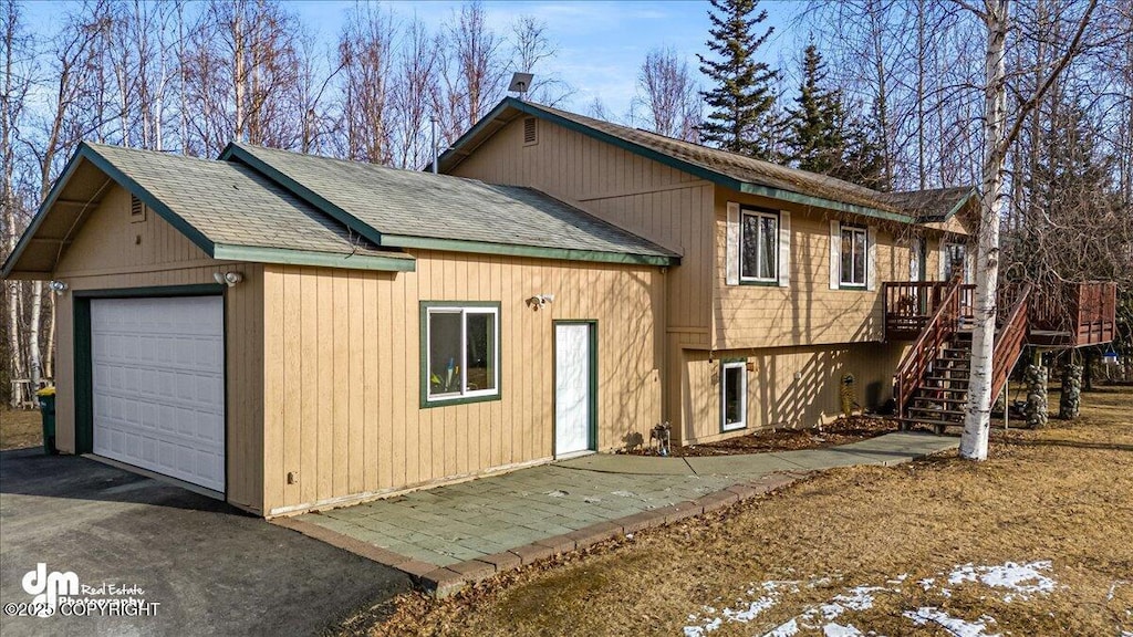 rear view of property with driveway, a shingled roof, stairs, a deck, and a detached garage