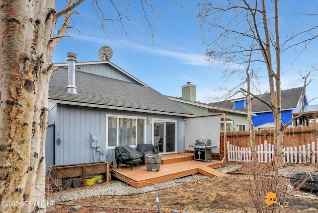 rear view of property featuring a shingled roof, a chimney, fence, and a deck