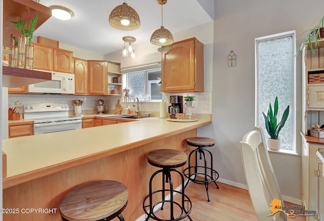 kitchen with a peninsula, white appliances, a sink, decorative backsplash, and a kitchen bar