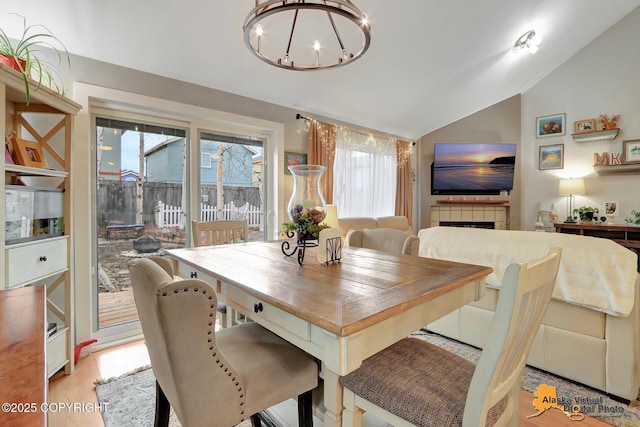 dining room featuring lofted ceiling, a tiled fireplace, a chandelier, and light wood-style floors