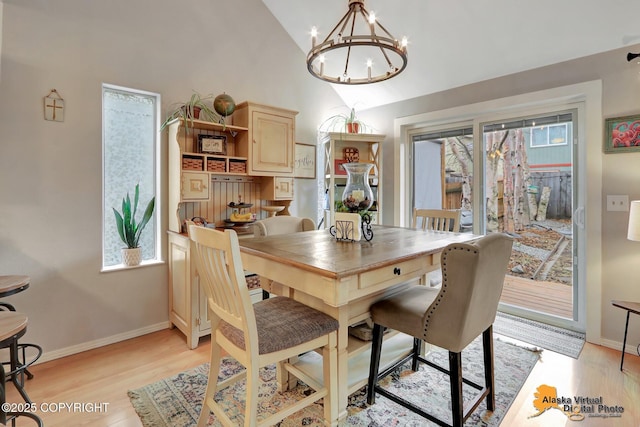 dining space featuring light wood-type flooring, lofted ceiling, baseboards, and an inviting chandelier