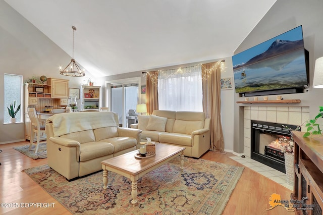 living area with light wood finished floors, a fireplace, high vaulted ceiling, and a chandelier