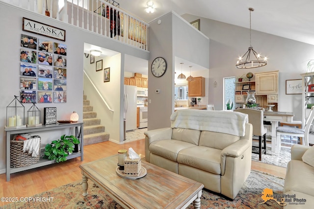 living room featuring a notable chandelier, light wood finished floors, high vaulted ceiling, baseboards, and stairs