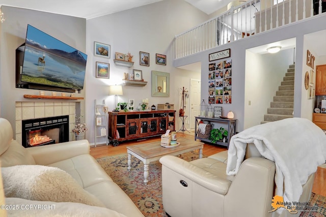 living area with stairs, high vaulted ceiling, a fireplace, and wood finished floors