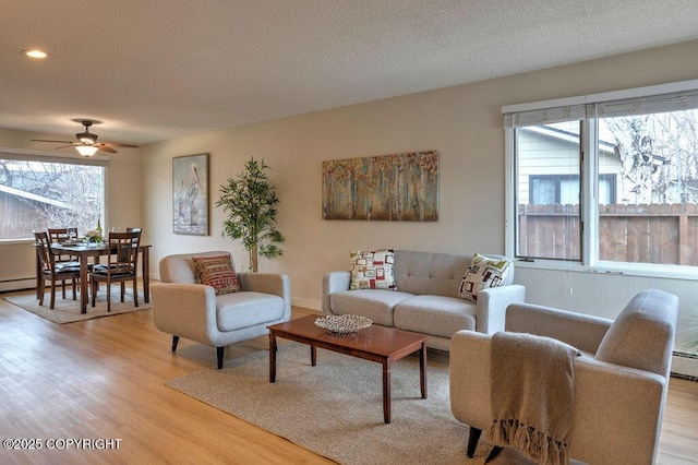 living area with light wood-type flooring, ceiling fan, a textured ceiling, and baseboards