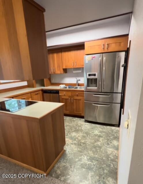 kitchen featuring brown cabinetry, appliances with stainless steel finishes, a peninsula, light countertops, and a sink