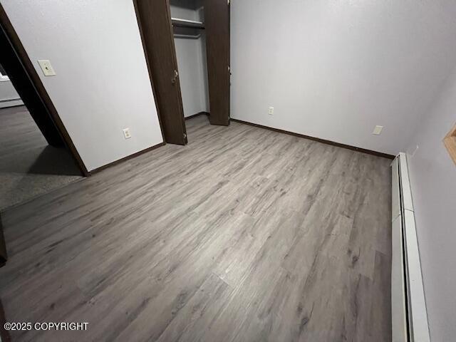 unfurnished bedroom with a baseboard radiator, a closet, light wood-style flooring, and baseboards