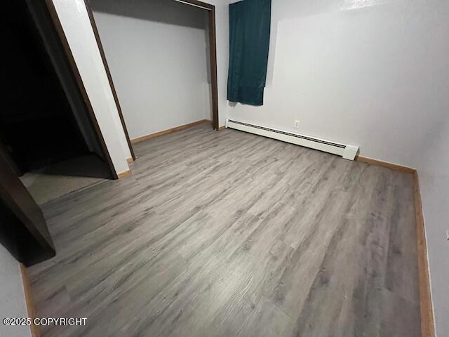 unfurnished bedroom with baseboard heating, wood finished floors, and baseboards