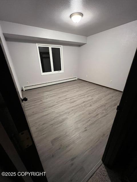 empty room featuring a textured ceiling, baseboard heating, and wood finished floors