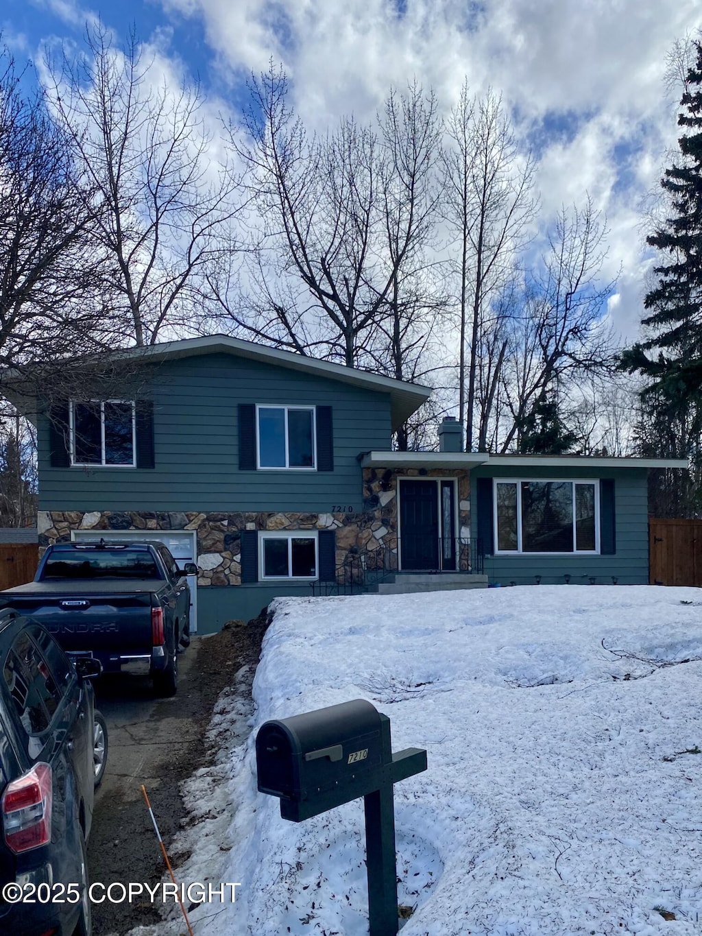 split level home featuring stone siding, fence, and a chimney