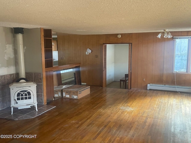 unfurnished living room featuring wood-type flooring, a wood stove, baseboard heating, and a textured ceiling