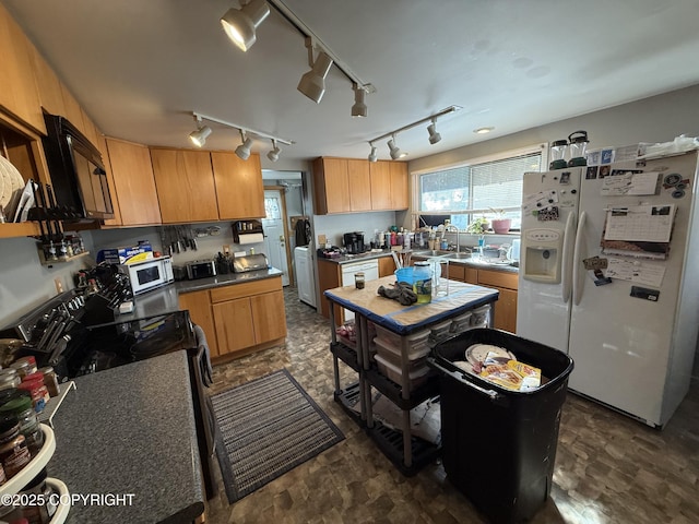 kitchen featuring a healthy amount of sunlight, white appliances, dark countertops, and a sink