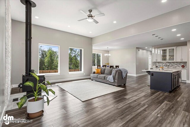 living area with recessed lighting, baseboards, dark wood finished floors, a wood stove, and ceiling fan with notable chandelier