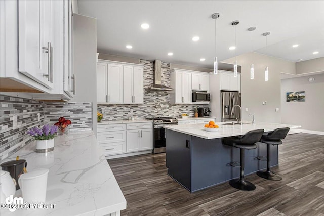 kitchen with tasteful backsplash, white cabinets, appliances with stainless steel finishes, wall chimney range hood, and a sink