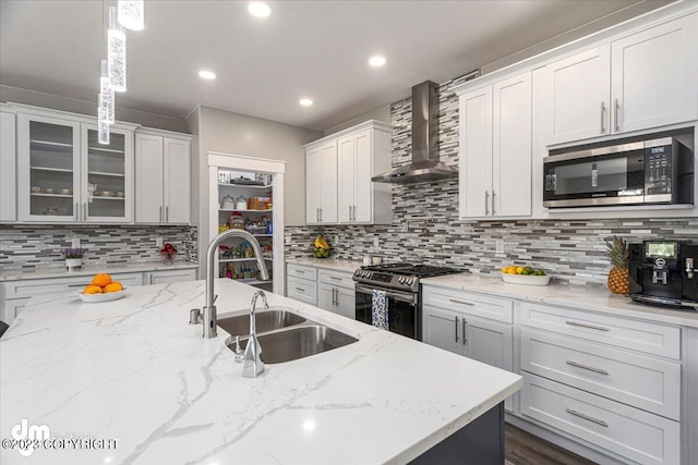 kitchen with tasteful backsplash, wall chimney exhaust hood, glass insert cabinets, stainless steel appliances, and a sink