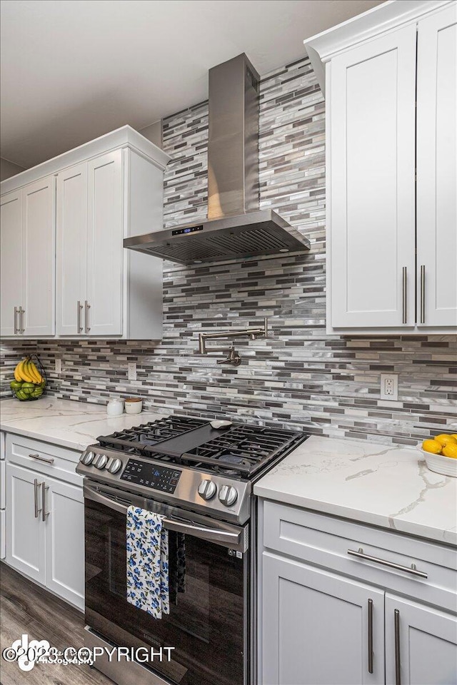 kitchen with wall chimney range hood, stainless steel range with gas cooktop, white cabinetry, and tasteful backsplash