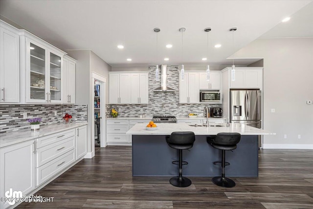 kitchen featuring a sink, white cabinets, appliances with stainless steel finishes, wall chimney exhaust hood, and a kitchen bar