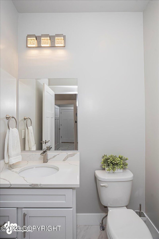 half bathroom featuring toilet, marble finish floor, baseboards, and vanity