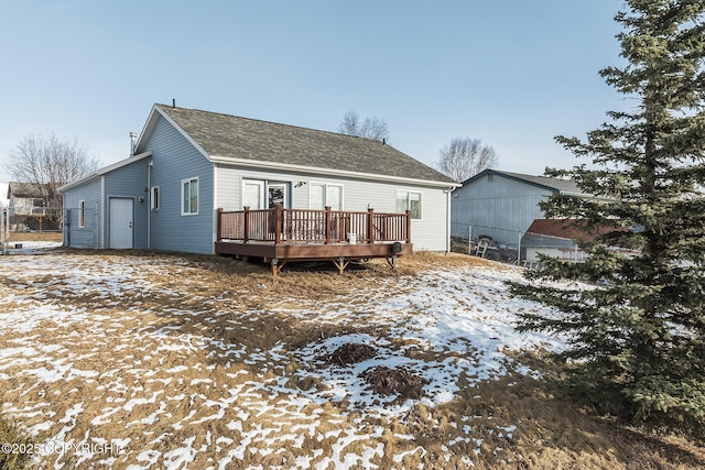 snow covered property with a wooden deck and a shingled roof