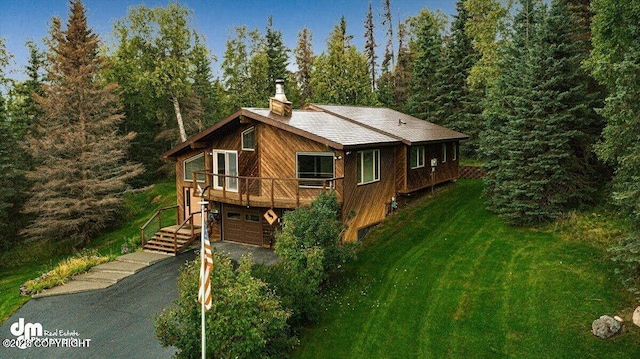 view of property exterior featuring a lawn, a deck, driveway, an attached garage, and a chimney