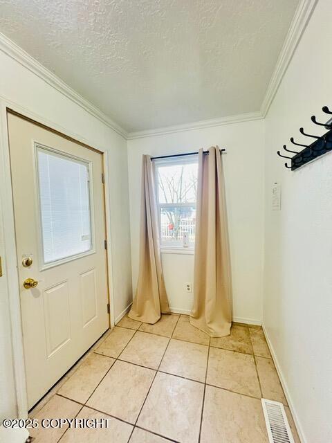 doorway to outside featuring crown molding, light tile patterned floors, visible vents, a textured ceiling, and baseboards