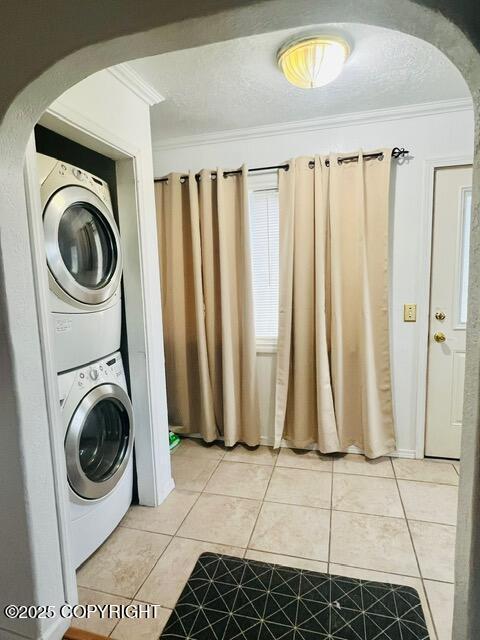 laundry area with laundry area, light tile patterned floors, arched walkways, stacked washer and clothes dryer, and ornamental molding