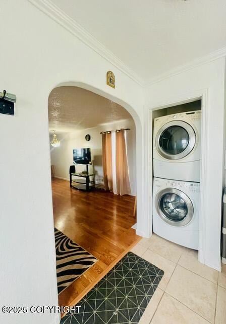 laundry area featuring arched walkways, light tile patterned floors, stacked washer and dryer, laundry area, and ornamental molding