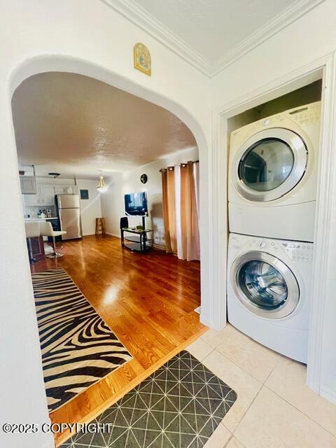 washroom featuring arched walkways, stacked washer / drying machine, ornamental molding, laundry area, and tile patterned floors