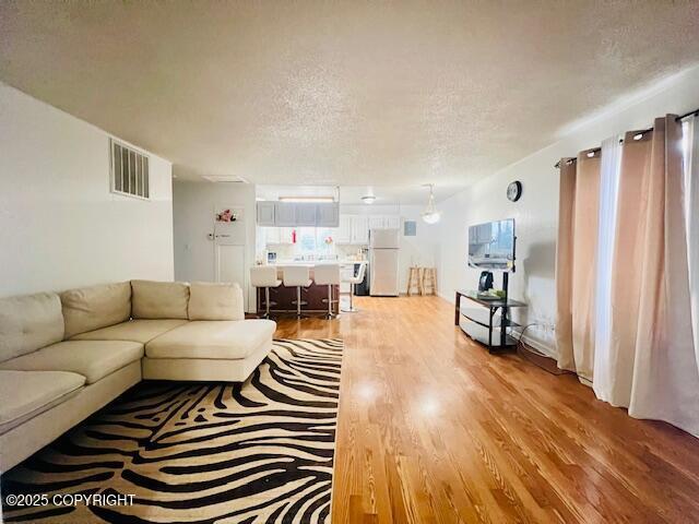 living area featuring a textured ceiling, visible vents, and wood finished floors