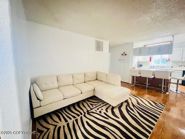 living room featuring a textured ceiling, visible vents, and wood finished floors