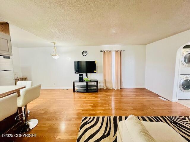 living room with light wood-style flooring, stacked washing maching and dryer, and a textured ceiling