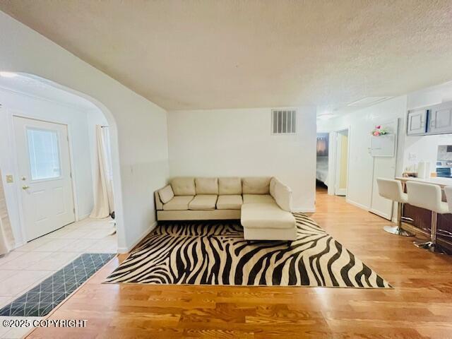 living room with arched walkways, visible vents, a textured ceiling, and wood finished floors