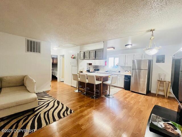 kitchen with visible vents, a kitchen breakfast bar, freestanding refrigerator, light countertops, and light wood-type flooring