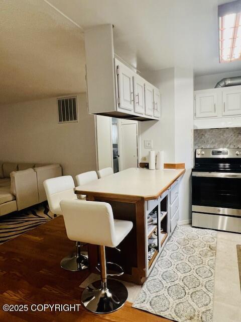 kitchen with tasteful backsplash, visible vents, a peninsula, stainless steel range with electric stovetop, and white cabinetry