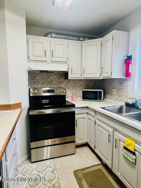 kitchen featuring stainless steel range with electric stovetop, under cabinet range hood, light countertops, and a sink